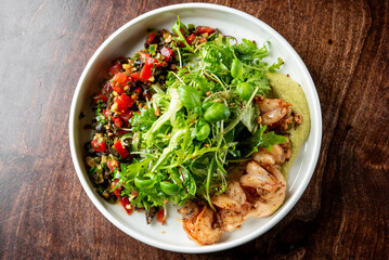 A vibrant seafood salad with grilled shrimp, mixed greens, and colorful vegetables in a white bowl