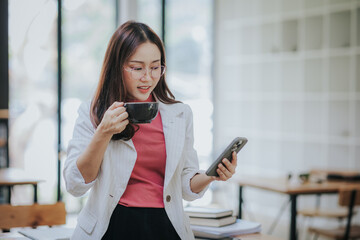 Beautiful Asian businesswoman holds a coffee cup and is drinking coffee in the morning before...