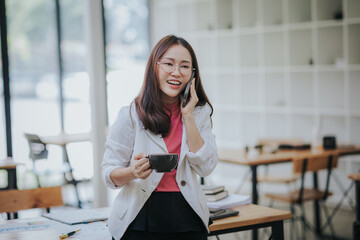 Beautiful Asian businesswoman holds a coffee cup and is drinking coffee in the morning before...