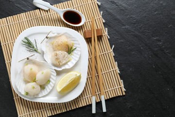 Raw scallops with green onion, rosemary, lemon and soy sauce on dark textured table, top view. Space for text