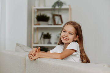 Adorable little girl with crossed arms sitting on a cozy couch, looking directly at the camera with...
