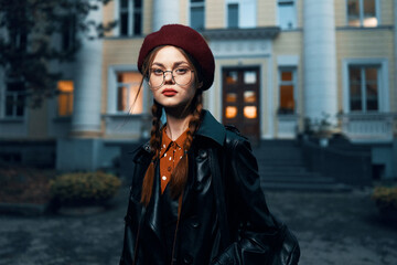 Obraz premium Stylish woman in red beret and glasses poses in front of historic brick building on urban street