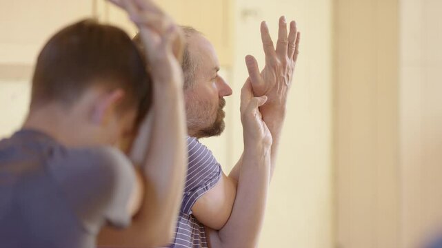 Yogi men in eagle pose gripping palm and thumb in yoga class, telephoto