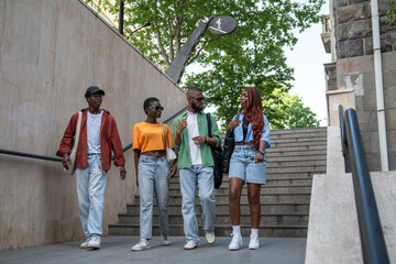 Obraz premium Group of stylish african american friends stroll through city streets, enter underpass, spend time with exciting conversations. Serious black students interested in dialogue communicate walks outside