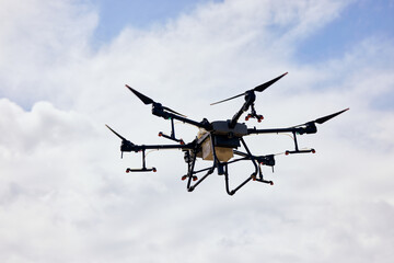 Close-up photo of an agrodrone flying in the sky over a field.