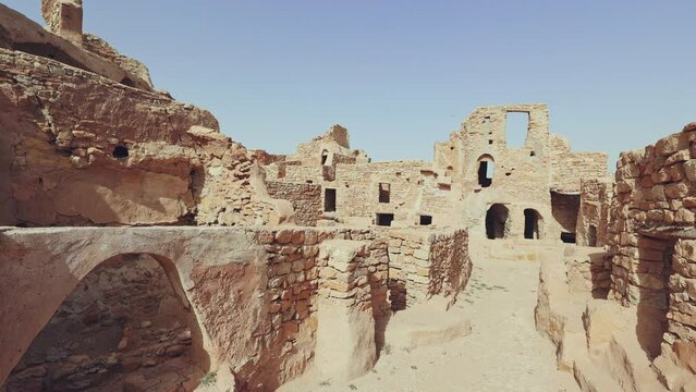 Eroded stone walls and arches of fortifications of Ksar Beni Barka standing under blue Tunisian sky, showcasing traditional Berber architecture in Tataouine