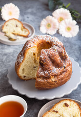 French Klouglof in a plate with its sliced piece and tea, flowers in background. It's a cake traditionally baked in a distinctive ring pan, similar to Bundt cake, but leavened with baker's yeast