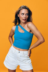 Stylish woman in blue top and white shorts posing confidently on vibrant orange background