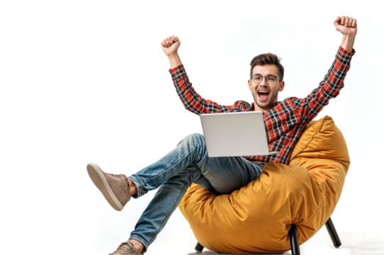 A young man in glasses, wearing a plaid shirt and jeans, sits on a yellow beanbag chair with a laptop, joyfully raising his arms, isolated on white or transparent png. The joy of working on a laptop.