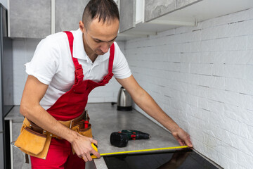 The carpenter places the induction hob in the space provided for the kitchen hob in the almost...