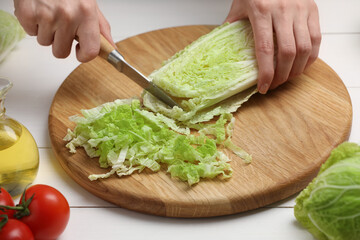 Woman cutting fresh chinese cabbage at white wooden table, closeup