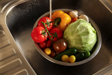 Washing different vegetables with tap water in metal colander inside sink
