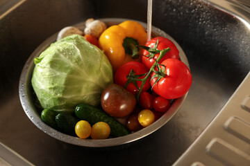 Washing different vegetables with tap water in metal colander inside sink