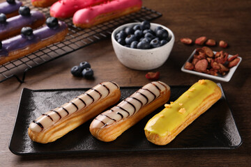 Different tasty glazed eclairs on wooden table, closeup