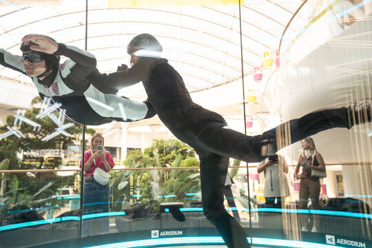 Excited teenage girl in helmet flying in aerodynamic tube wind tunnel. Skydiving training.