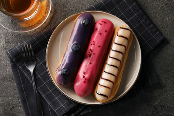 Different tasty glazed eclairs served with tea on grey textured table, flat lay