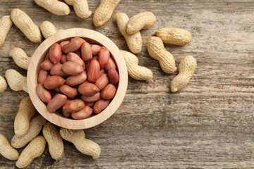Fresh unpeeled peanuts in bowl on wooden table, top view. Space for text