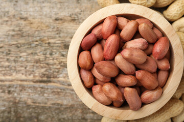Fresh unpeeled peanuts in bowl on wooden table, top view. Space for text