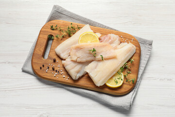 Pieces of raw cod fish, lemon and spices on white wooden table, top view