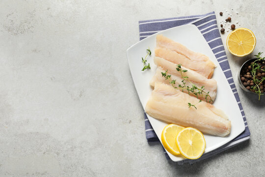 Pieces of raw cod fish, peppercorns and lemon on light grey table, top view. Space for text