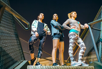 Three athletic women standing on urban stairs at night ready for an evening exercise session in the...