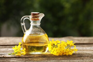 Rapeseed oil in glass jug and beautiful yellow flowers on wooden table outdoors