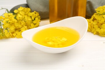 Rapeseed oil in gravy boat and beautiful yellow flowers on white wooden table