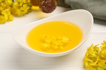 Rapeseed oil in gravy boat and beautiful yellow flowers on white wooden table, closeup