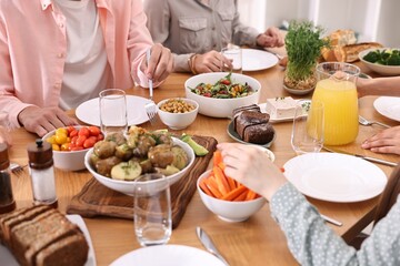 Friends eating vegetarian food at wooden table indoors, closeup