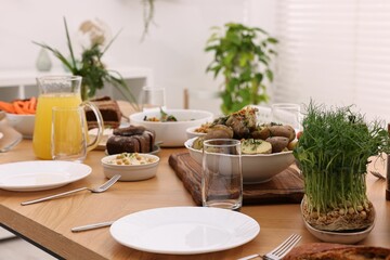 Healthy vegetarian food, jug of juice, cutlery, glasses and plates on wooden table indoors