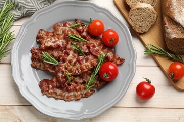 Slices of tasty fried bacon with rosemary and tomatoes served on wooden table, flat lay