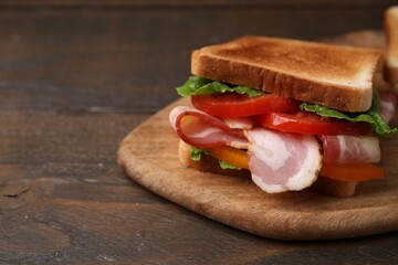 Tasty sandwich with bacon and tomato on wooden table, closeup. Space for text
