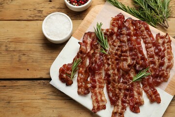 Slices of tasty fried bacon, rosemary and salt on wooden table, top view