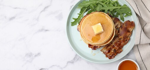 Tasty pancakes with butter, fried bacon and fresh arugula on white marble table, flat lay with space for text. Banner design