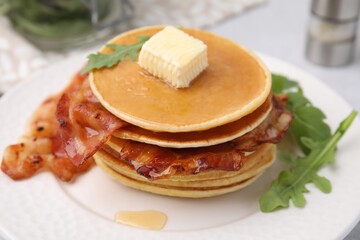 Delicious pancakes with bacon, butter and arugula on table, closeup