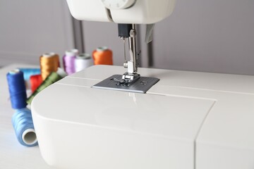 Sewing machine and spools of threads on white table indoors, closeup