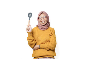 Smilling beautiful Asian woman holding spoon while doing housework isolated over white background