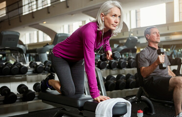 Fototapeta na wymiar Workout, weights and senior woman in gym for fitness, training and cardio exercise with music. Retirement, sports and person with dumbbells for wellness, muscle strength and mobility for health
