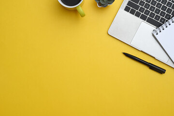Laptop, notebook, pen and coffee cup on yellow background with copy space