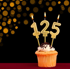 Birthday candle with cupcake - Number 125 on black background with out of focus lights