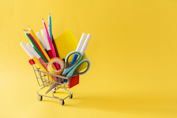School and office supplies in shopping cart on yellow background