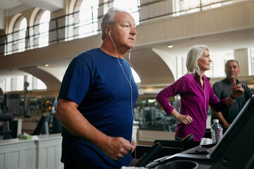 Earphones, treadmill and senior man running in gym for workout, physical health and wellness in retirement. Male person, running or training listening to podcast for cardio, walking and fitness
