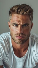 Fototapeta premium Handsome confident blond man, staring serious and cool at camera, wearing white t-shirt, white background