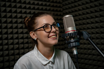 confident girl in glasses stands poised in a broadcasting studio before microphone in the acoustic...