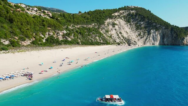 A panoramic aerial view of Milos Beach, a picturesque beach on Lefkada Island, Greece, with turquoise water, white sand, and a boat in the distance.