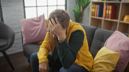 Man in despair sitting on a sofa indoors, covering face with hands, showing stress, sadness or depression.