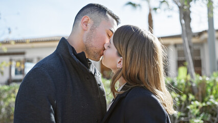 A loving couple kisses on a sunny city street, portraying affection and romance in an urban outdoor setting.