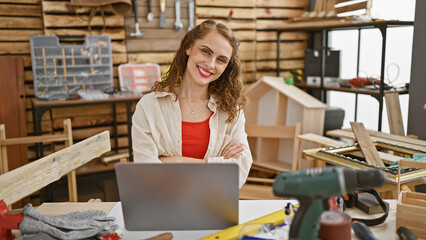 Smiling young woman carpenter engrossed in her online carpentry business, sitting at a table with...