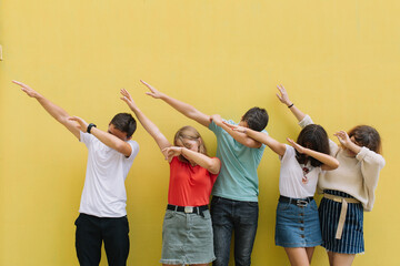 Fototapeta premium Summer holidays and teenage concept - group of smiling teenagers cover their faces with their hands on a yellow wall background
