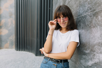 Pretty teen girl with braces in glasses posing near gray wall